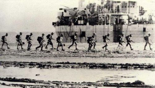 Pasukan TNI berjalan di pinggir pantai Dili, dengan latar KRI Teluk Bone.